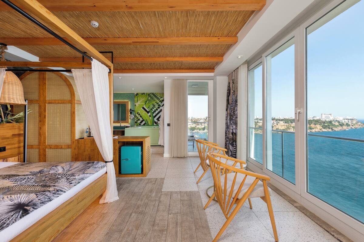A bedroom with a bed, wooden furniture, a small table, and a view of the sea.