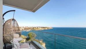 Un balcón con una silla de mimbre, una pequeña mesa y vistas al mar y a una costa lejana.
