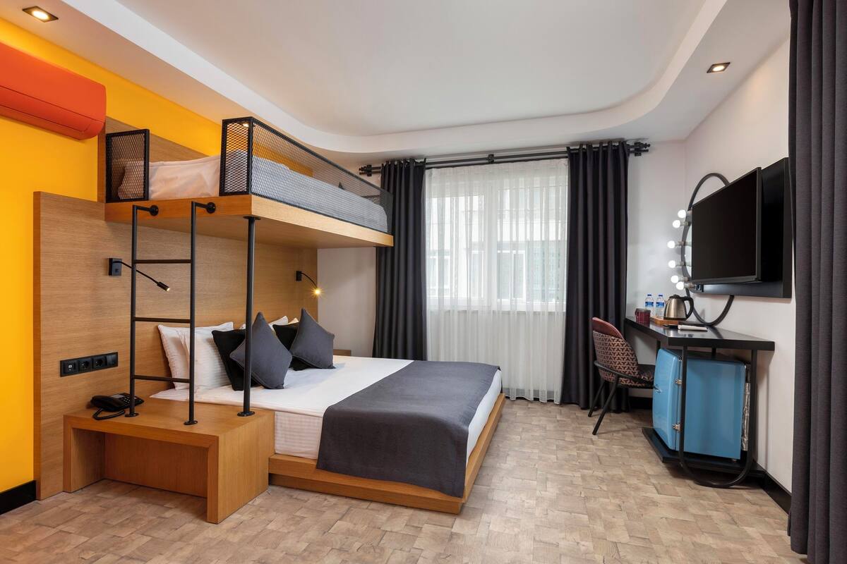 A modern hotel room with a bunk bed, a desk with a mirror, and a television.