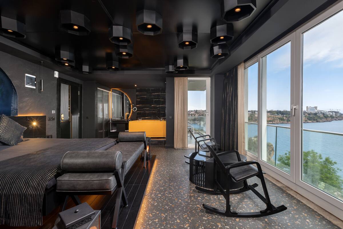 A modern bedroom with a large bed, a desk, and a view of a body of water.