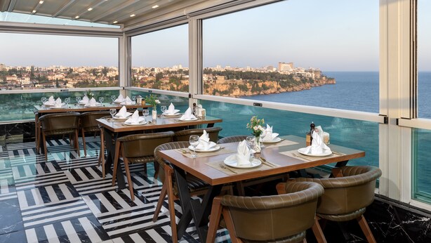 Un restaurante con mesas dispuestas para comer, con vista a un paisaje urbano costero.