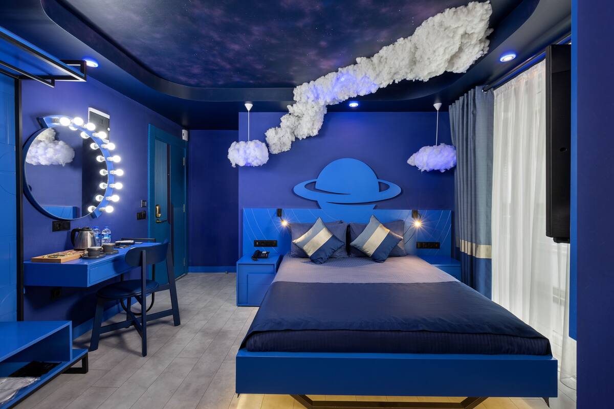 A bedroom with a bed, a desk, and a vanity with lights.