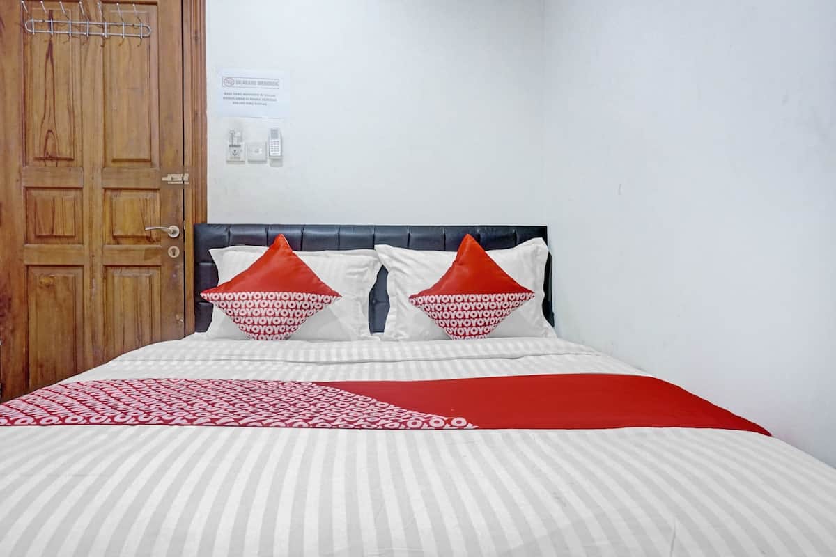 A hotel room with a wooden door, a bed with striped bedding, and two red and white pillows.