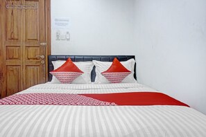 Una habitació d'hotel amb una porta de fusta, un llit amb roba de llit a ratlles i dos almoinos vermells i blancs.