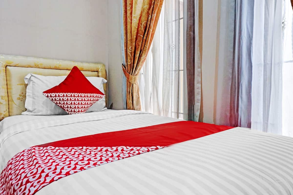 A neatly made bed with a white and red patterned bedspread, a red pillow, and a white pillow with a red and white pattern.