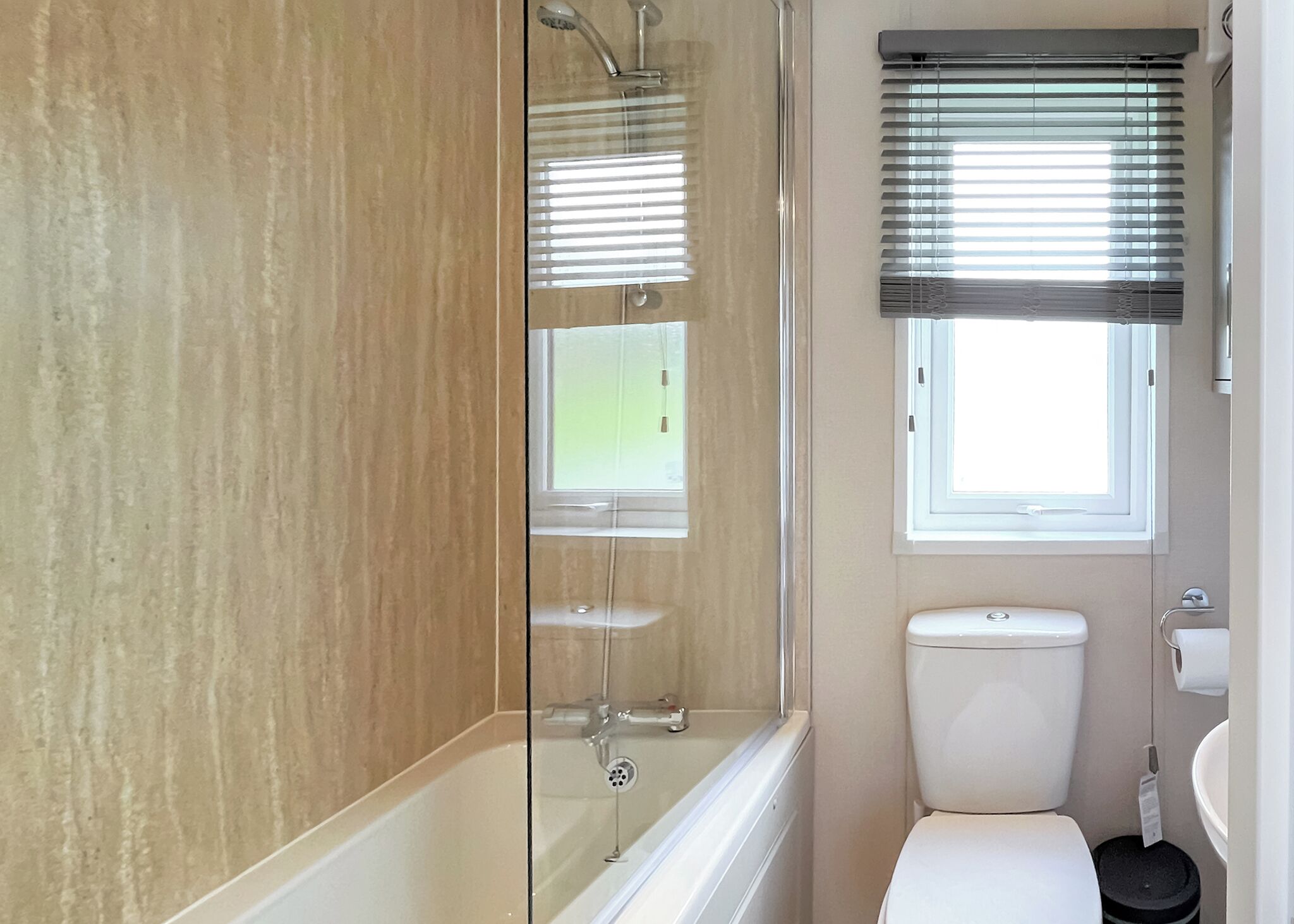 Un baño con bañera, inodoro y ventana con persianas.
