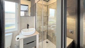 Une salle de bain moderne avec un lavabo blanc, un miroir au-dessus, une douche avec des portes en verre et des toilettes.