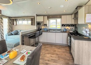 A modern kitchen with a central island, a dining area with a sofa, and breakfast items on the table.