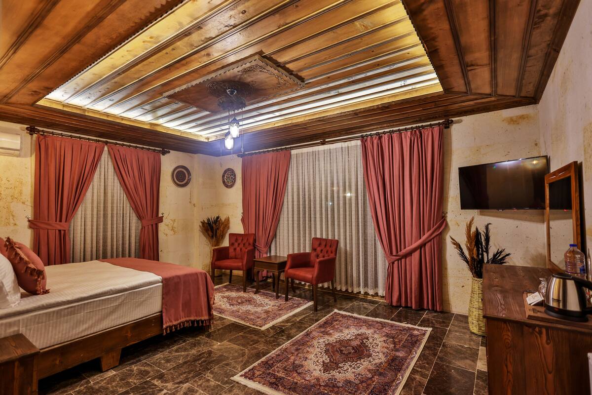 Una habitación de hotel con una cama, dos sillas, una mesita, un televisor y un ventilador de techo.