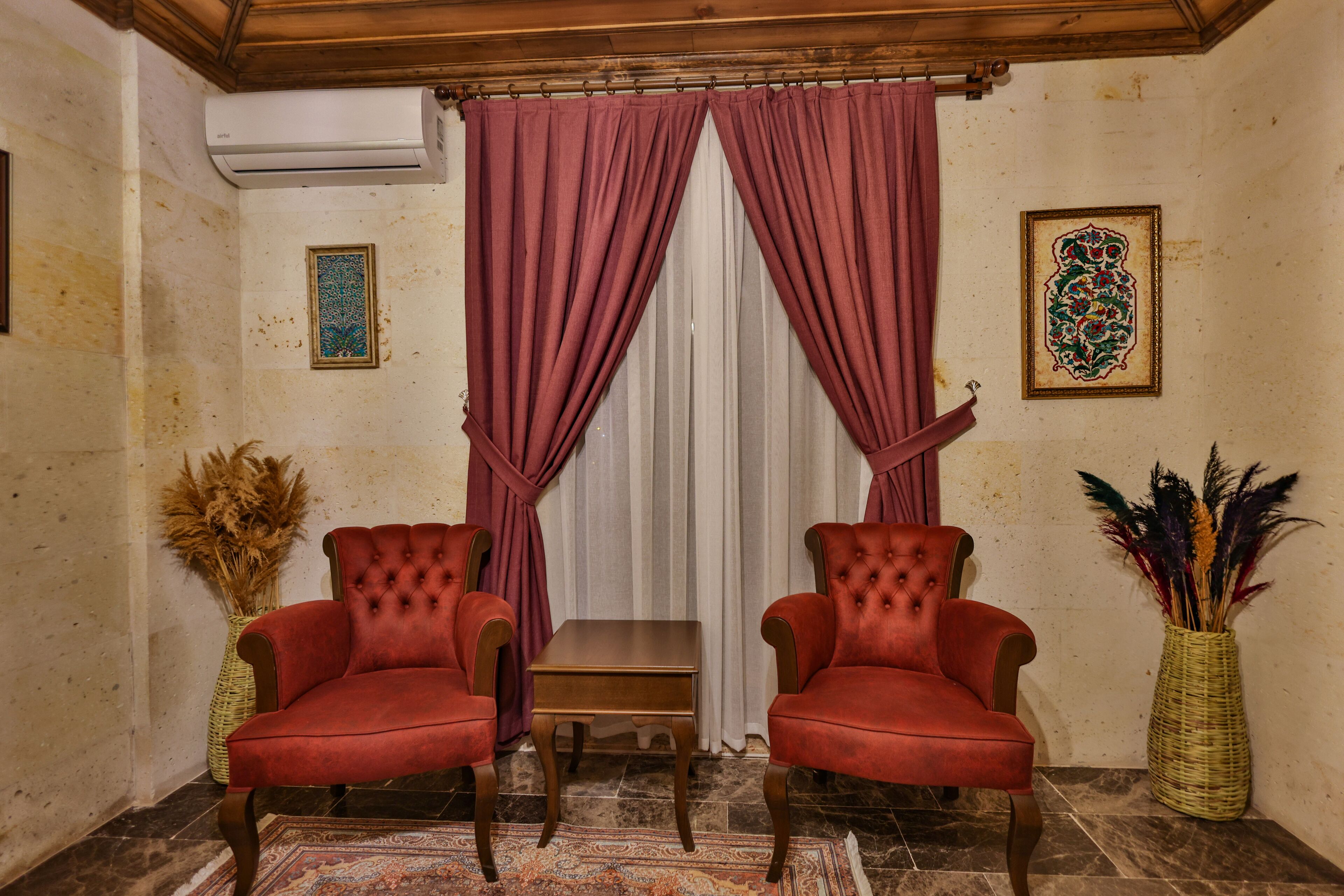 A room with two red upholstered chairs, a small wooden table, a patterned rug, and decorative vases.