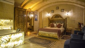 Quarto com banheira de mármore, cama com cabeceira estampada e área de estar com cadeiras azuis.