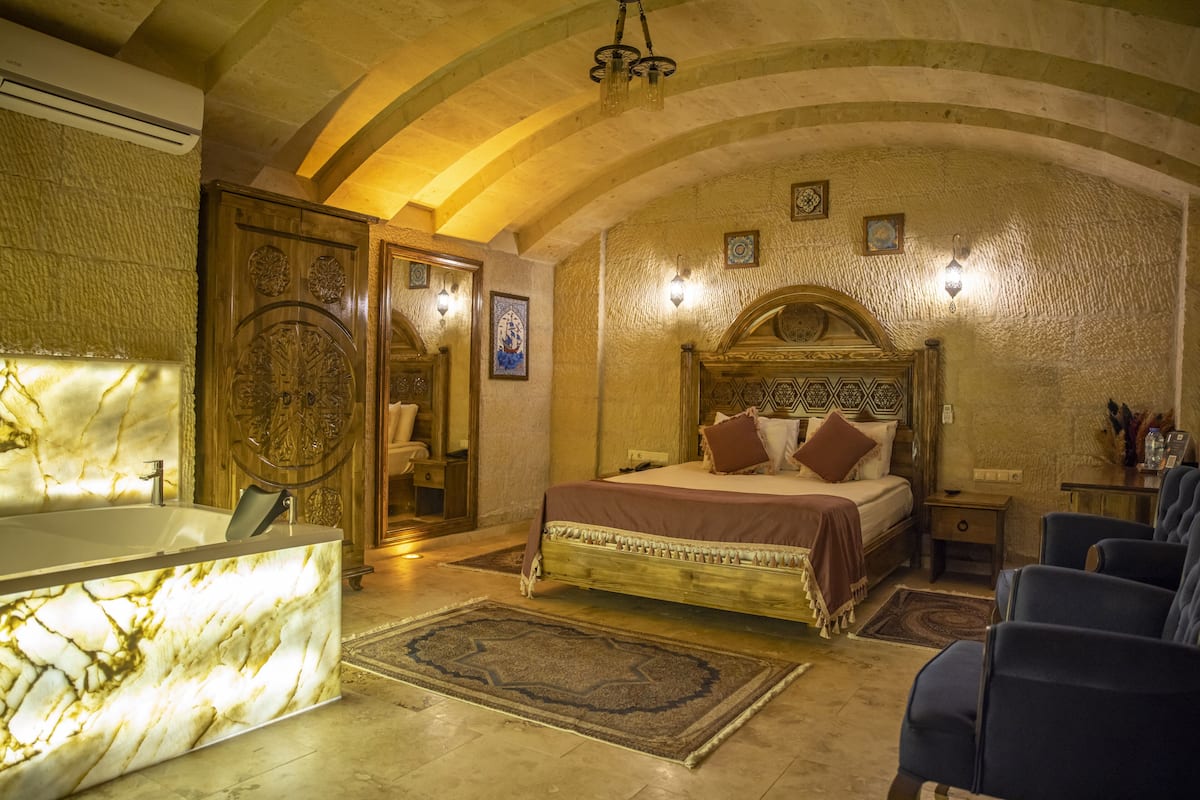 Una habitación con una bañera de mármol, una cama con un cabecero estampado y una zona de estar con sillas azules.