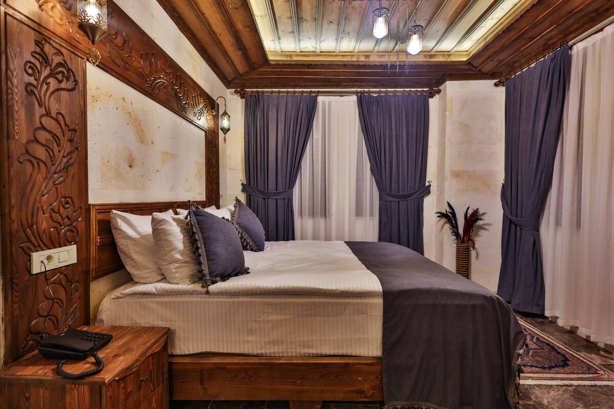 Un dormitorio con cabecera de madera, una cama con ropa de cama blanca y oscura, y una mesita de noche con un teléfono.