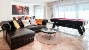Un salon avec une table de billard, un canapé en cuir et une grande fenêtre.