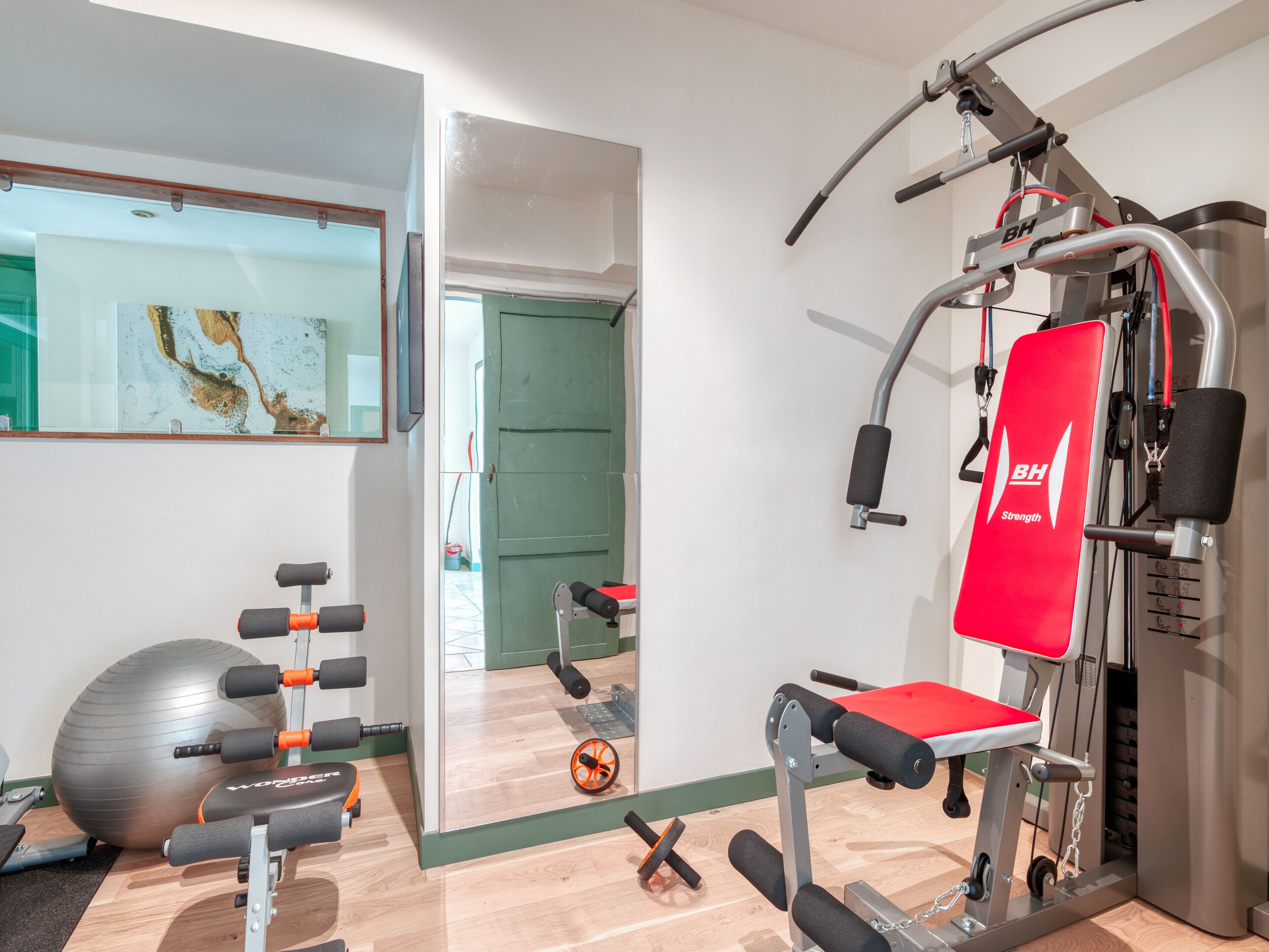 Un gimnasio con equipo de ejercicio, una pelota grande y un espejo en la pared.