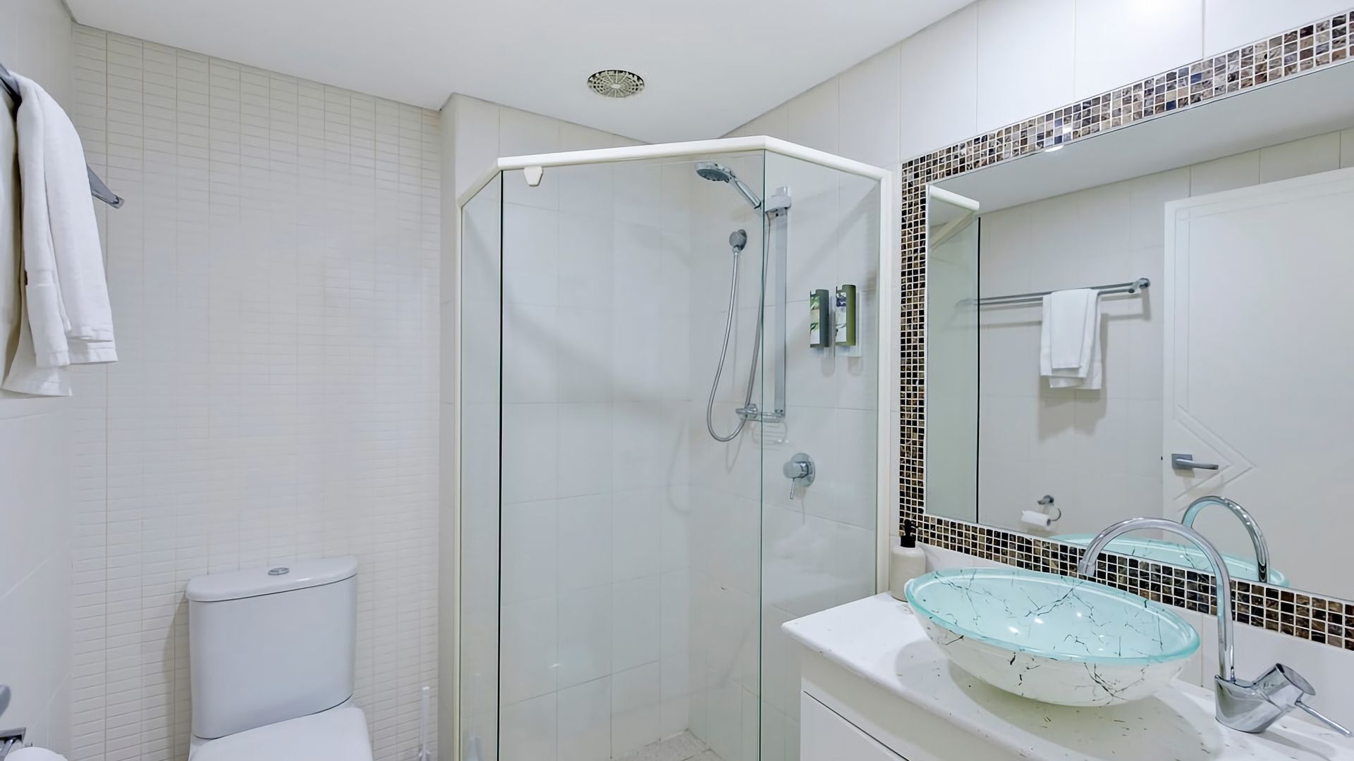 A modern bathroom with a glass-enclosed shower, a white toilet, and a sink with a glass basin.