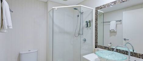 A modern bathroom with a glass-enclosed shower, a white toilet, and a sink with a glass basin.