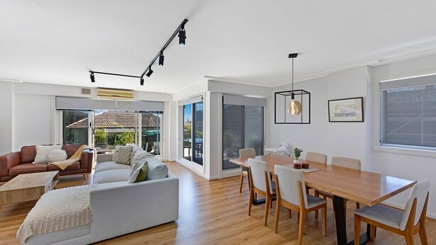 A modern living room with a sofa, a dining table with chairs, and a large window.