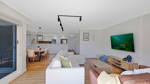 A modern living room with a sofa, a TV, and a dining area with chairs and a table.