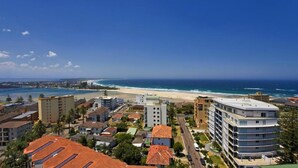 A coastal cityscape with a beach, residential buildings, and a prominent hotel with a rooftop terrace.