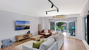 A modern living room with a flat-screen TV, a sofa, a coffee table, and a sliding glass door leading to an outdoor area.