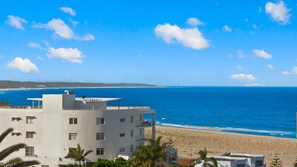 Un hotel frente a la playa con varios pisos, balcones y vistas al océano.
