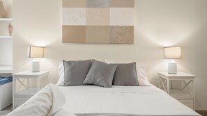 Una cama bien hecha con almohadas, dos mesitas de noche con lámparas y una pared con un diseño geométrico.