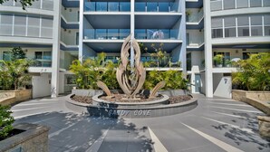 Un edificio moderno con una escultura central, un letrero que dice 'SANDY COVE' y follaje circundante.