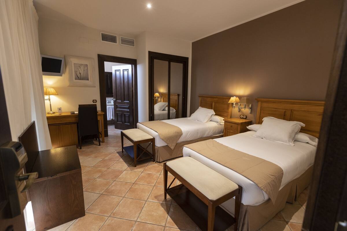 A hotel room with two beds, a desk, a chair, and a TV.