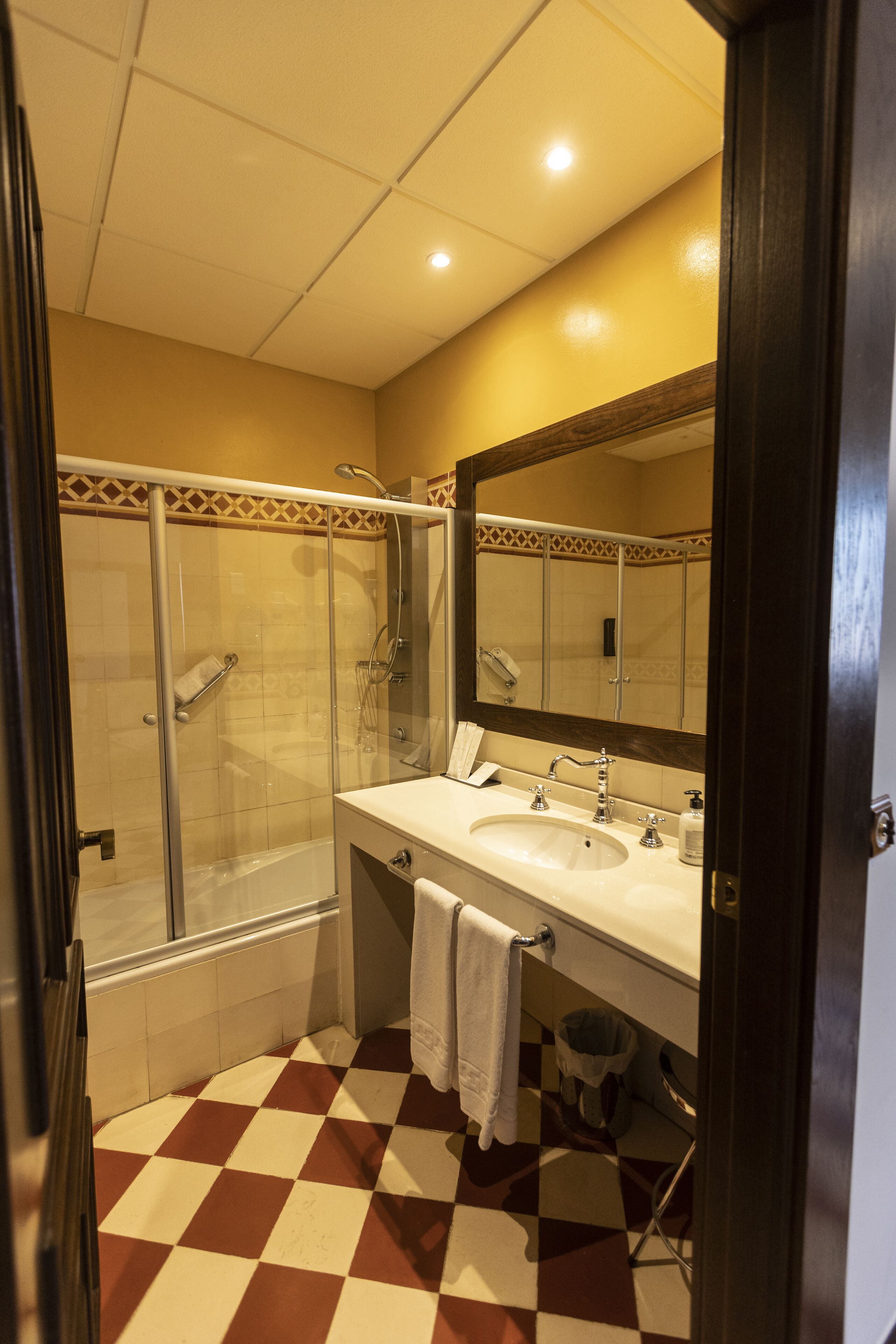 Un baño con piso a cuadros, un lavamanos, un espejo y una zona de ducha.