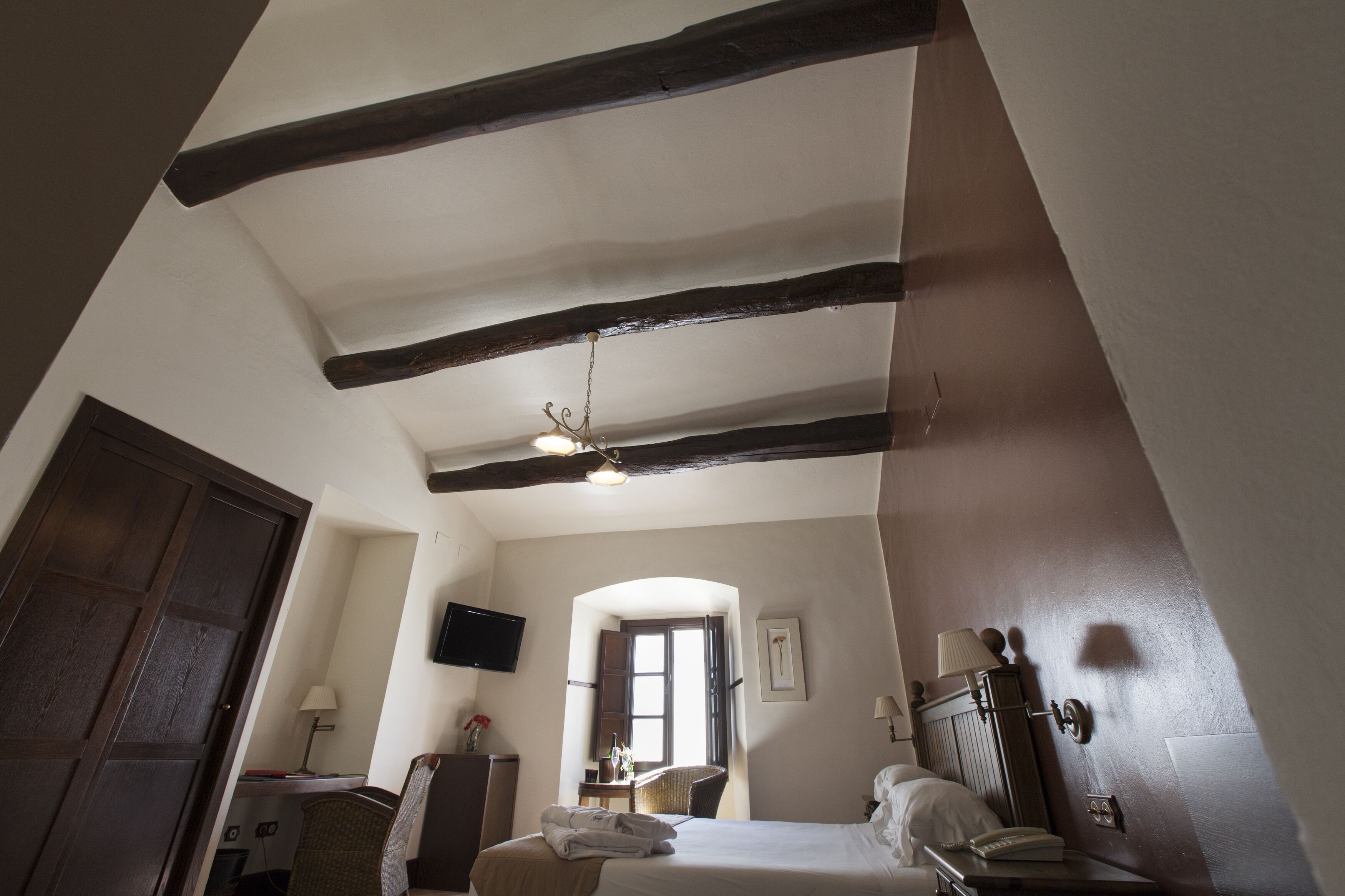 Une chambre d’hôtel avec des poutres apparentes, un lit, un bureau, une chaise, un téléviseur et une porte.