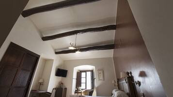Une chambre d’hôtel avec des poutres apparentes, un lit, un bureau, une chaise, un téléviseur et une porte.