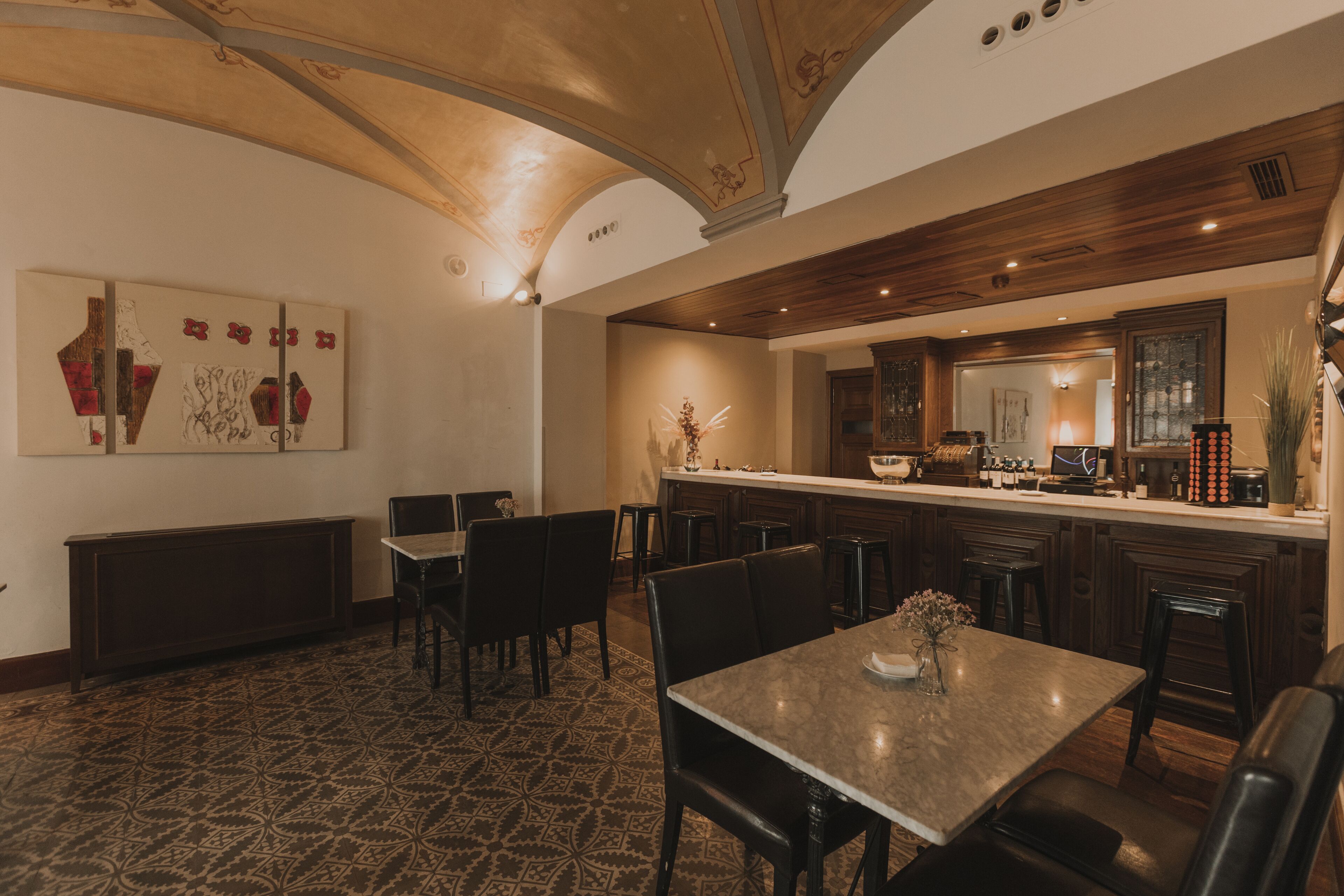 A dining area with a patterned floor, a central table with chairs, and a bar area with stools.