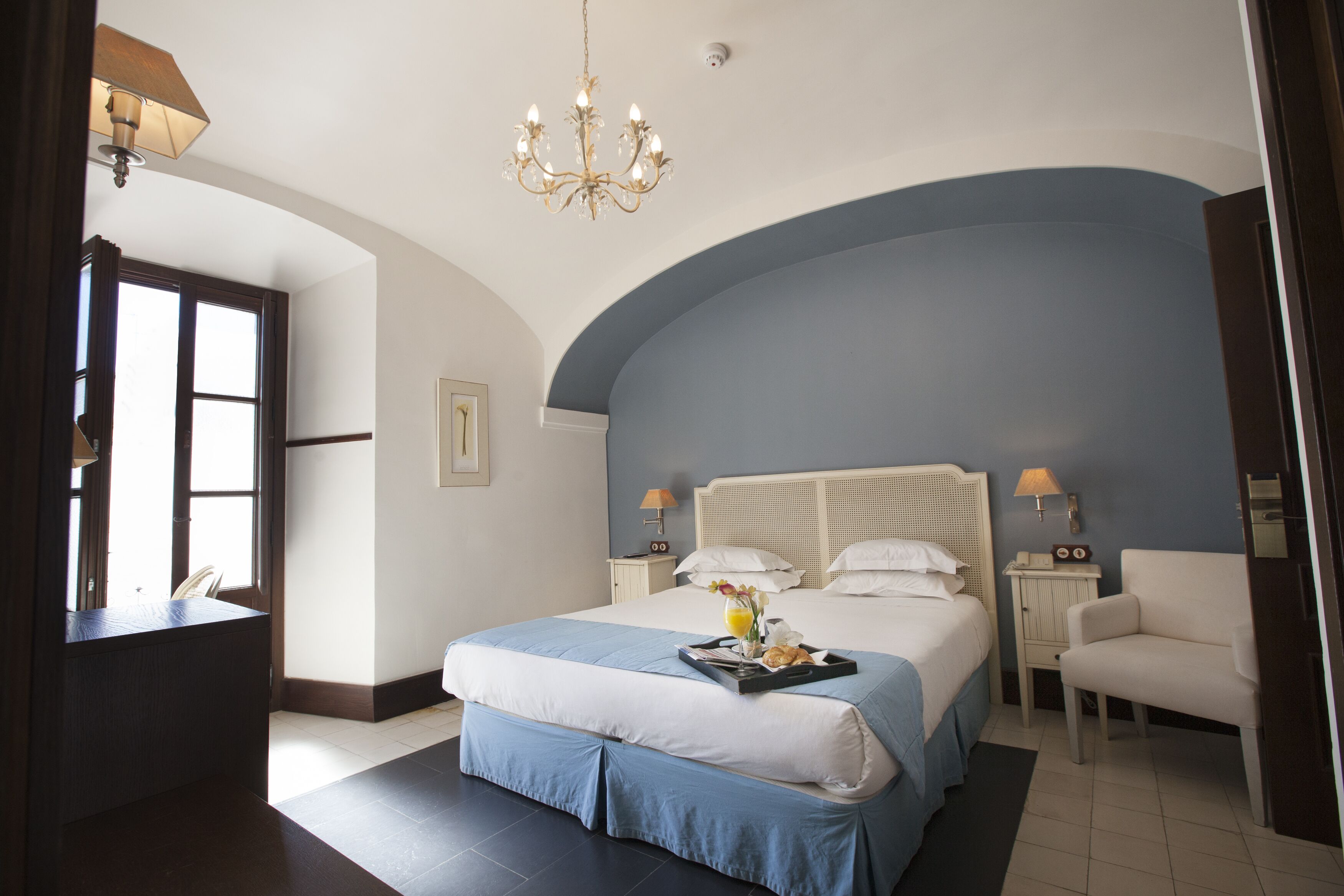 Habitación de hotel con una cama grande, un escritorio, una silla y una araña.