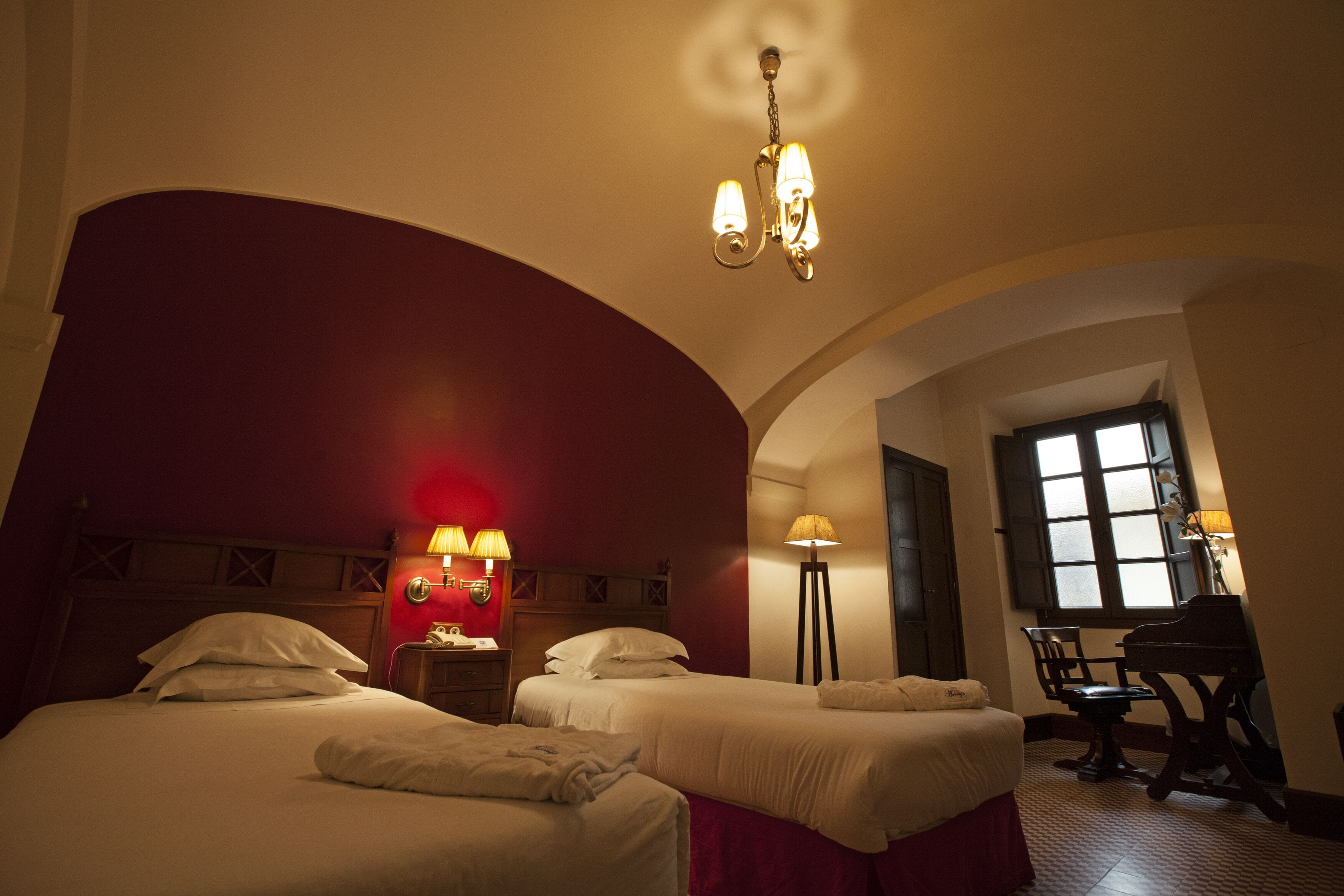 Una habitación de hotel con dos camas, un piano, un escritorio y un ventanal grande.