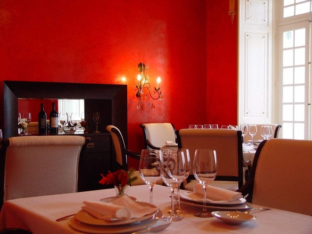 A dining area with a red wall, a chandelier, and a table set for two.