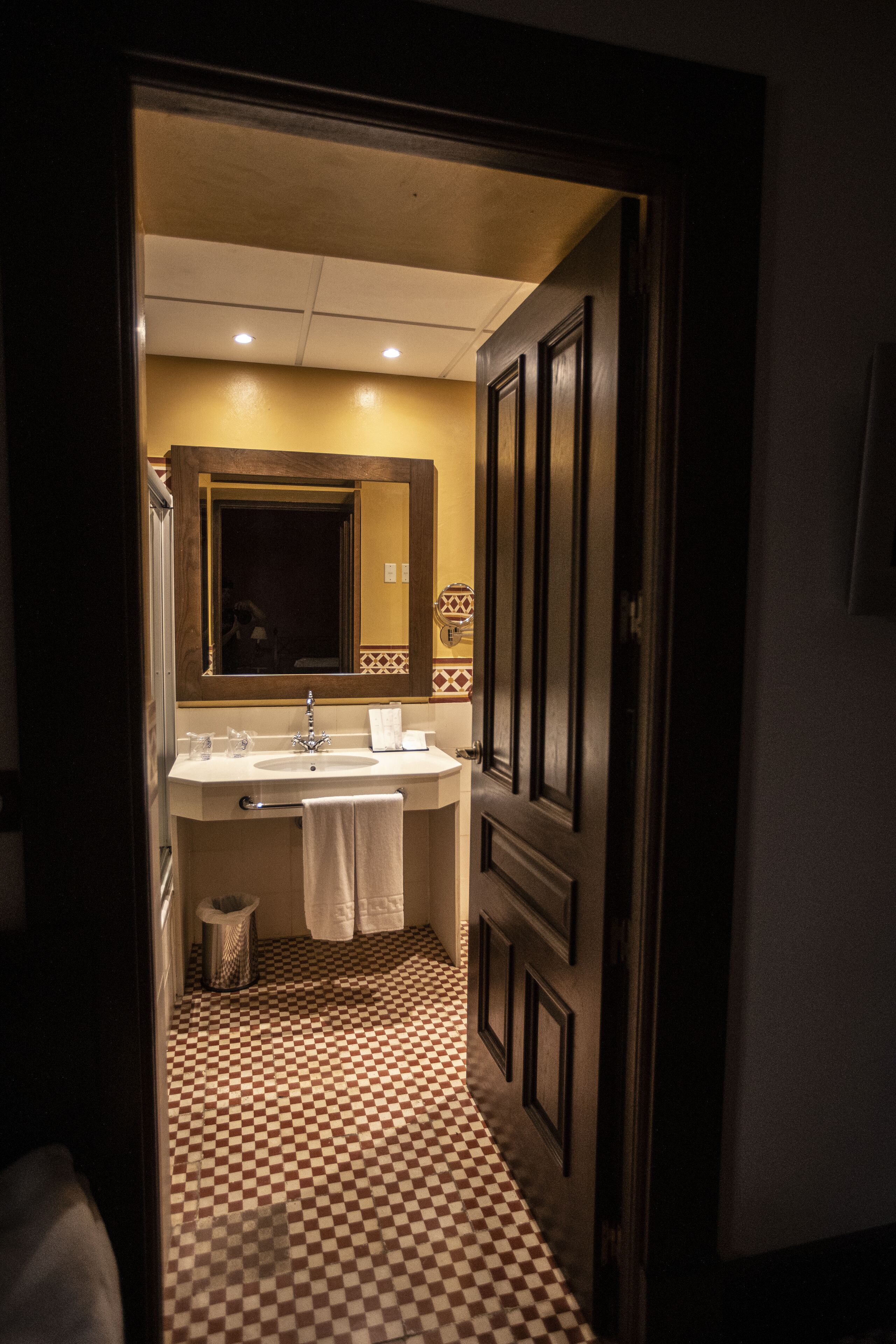 Een hotelbadkamer met een zwart-wit geruite vloer, een wastafel, een spiegel en een deur.