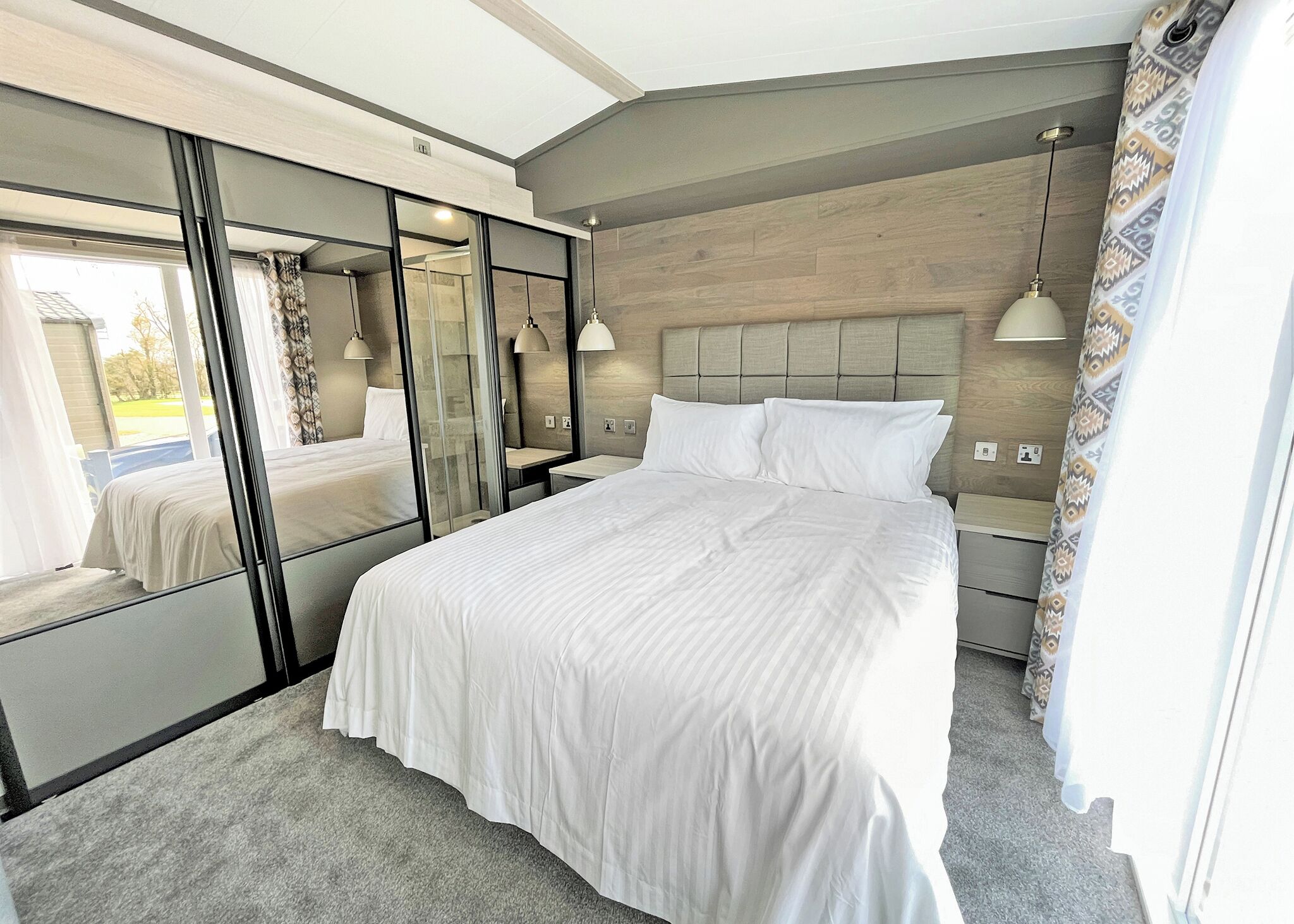 Une chambre avec un grand lit, un miroir, une table de chevet et une fenêtre.