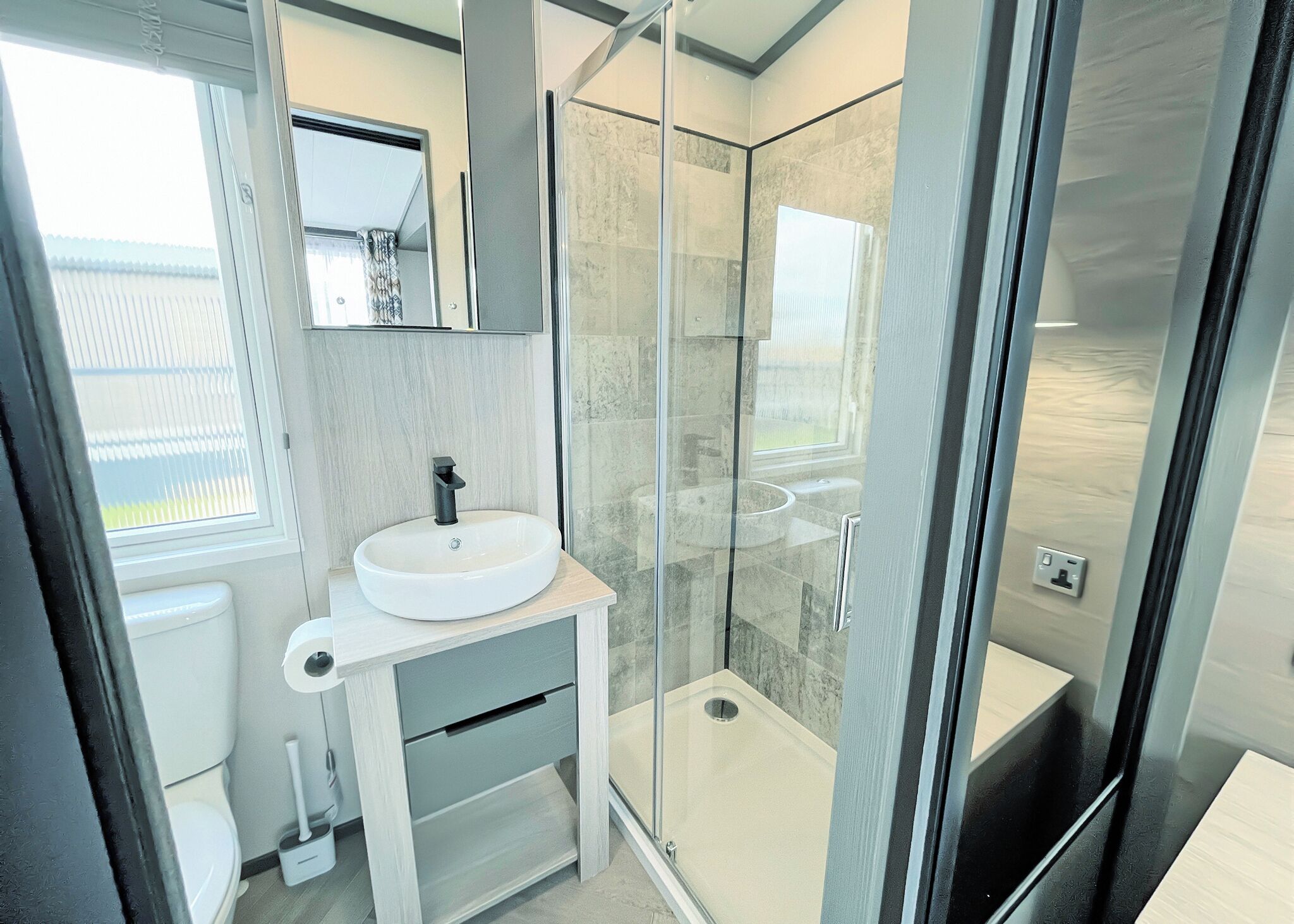 Une salle de bain moderne avec une douche à parois de verre, un lavabo blanc et un miroir au-dessus.