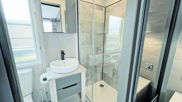 Une salle de bain moderne avec une douche à parois de verre, un lavabo blanc et un miroir au-dessus.