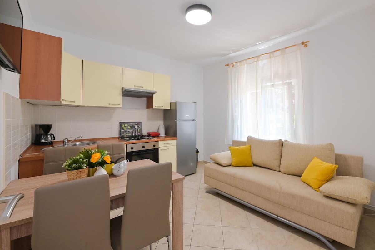 Una cocina compacta con comedor, un sofá con cojines amarillos y una ventana con cortinas de encaje.