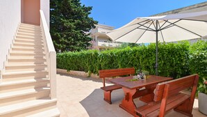 A staircase leading to a building, a wooden bench, a picnic table, and a large umbrella. - Apartments Ena (Novalja)