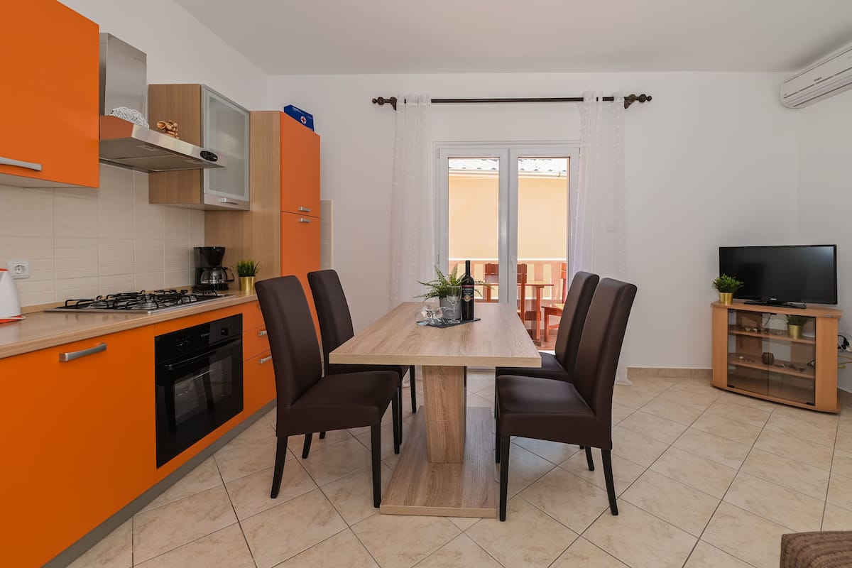Una cocina moderna con armarios color naranja, una isla central y un comedor con cuatro sillas.