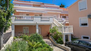 A two-story residential building with balconies, a car parked in front, and a garden area. - Apartments Ena (Novalja)