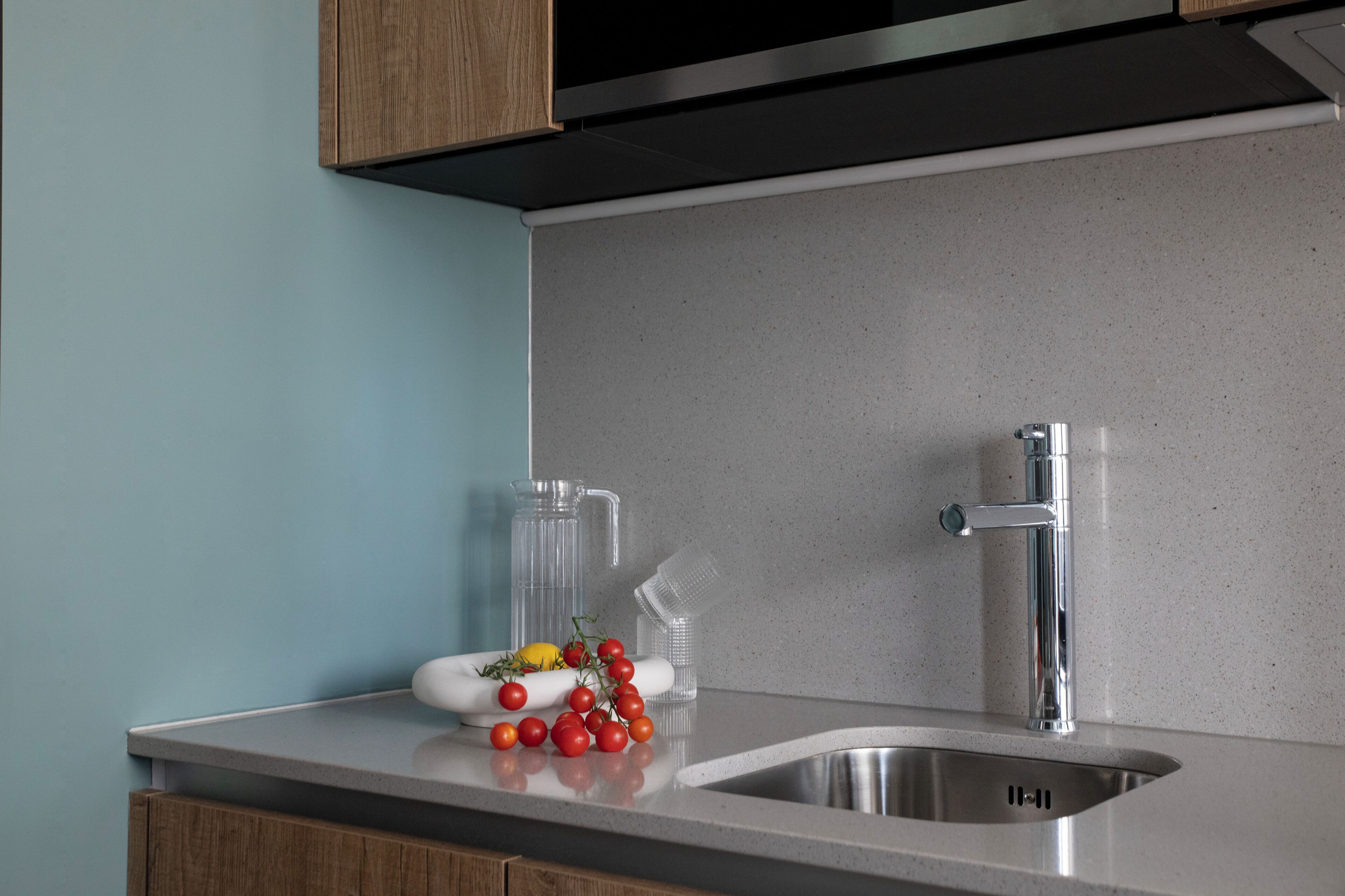 A kitchen with a stainless steel sink, a clear glass pitcher, and a white soap dish with a lemon and tomatoes.