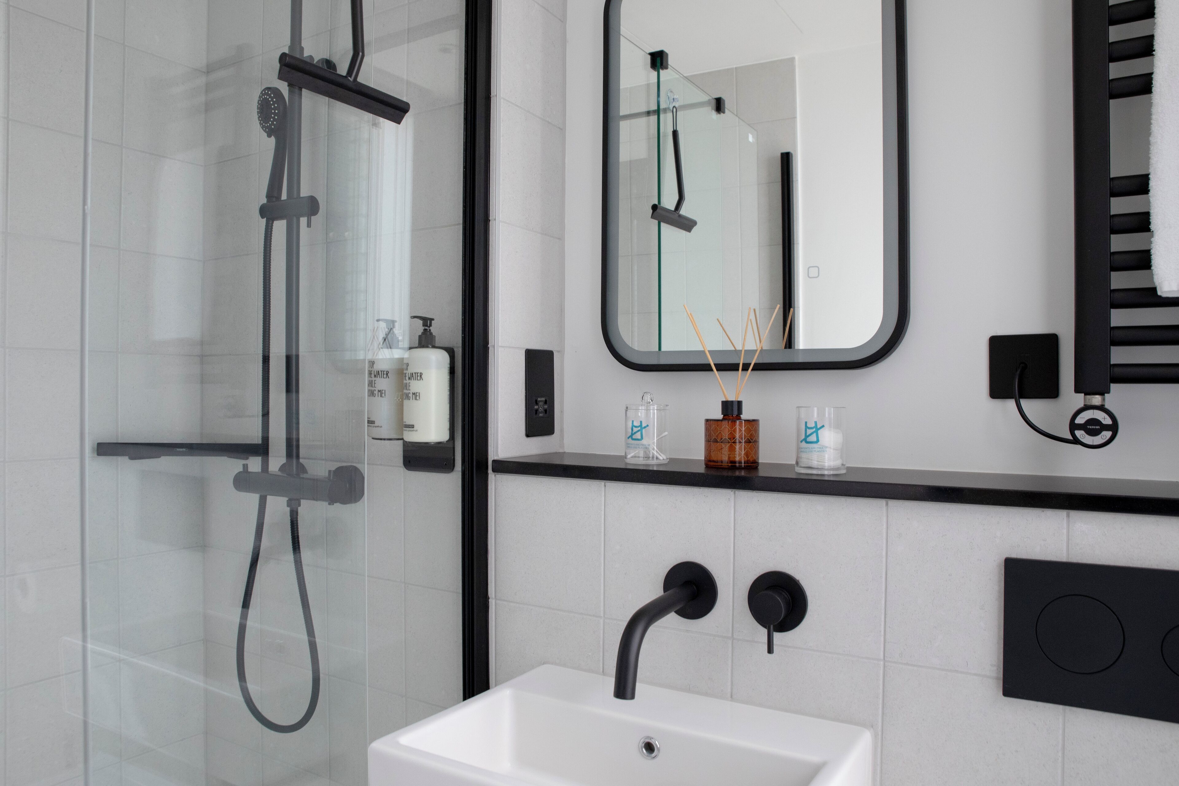 Un bany modern amb plat de dutxa envoltat de vidre, un lavabo blanc, un aixeta negra i un mirall sobre el lavabo.