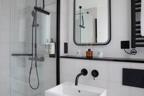 A modern bathroom with a glass-enclosed shower, a white sink, a black faucet, and a mirror above the sink. - Bob W London Tower Hill - Studios (London)