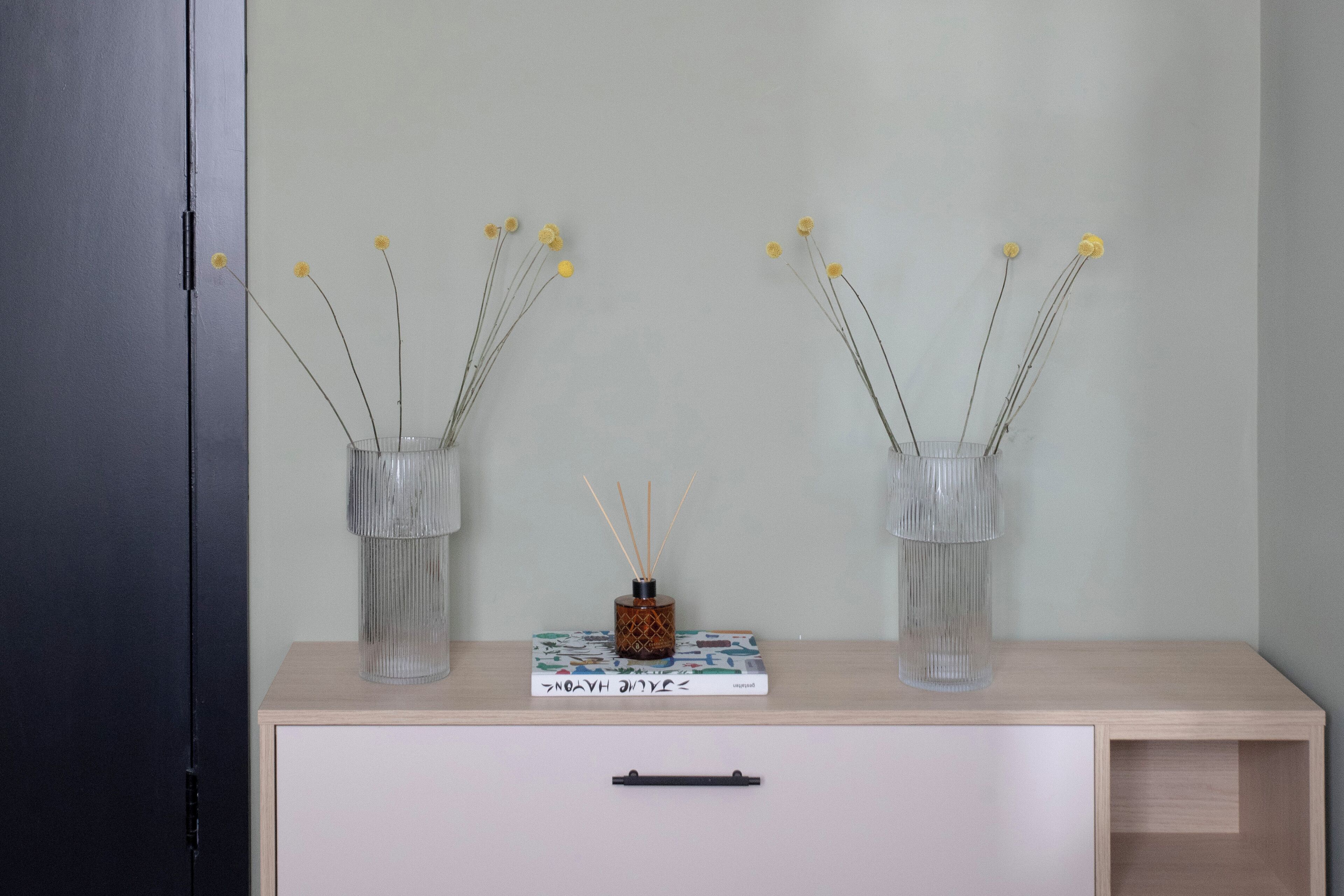 Une pièce avec un bureau en bois, deux vases transparents contenant des fleurs jaunes, un livre et un petit objet décoratif.