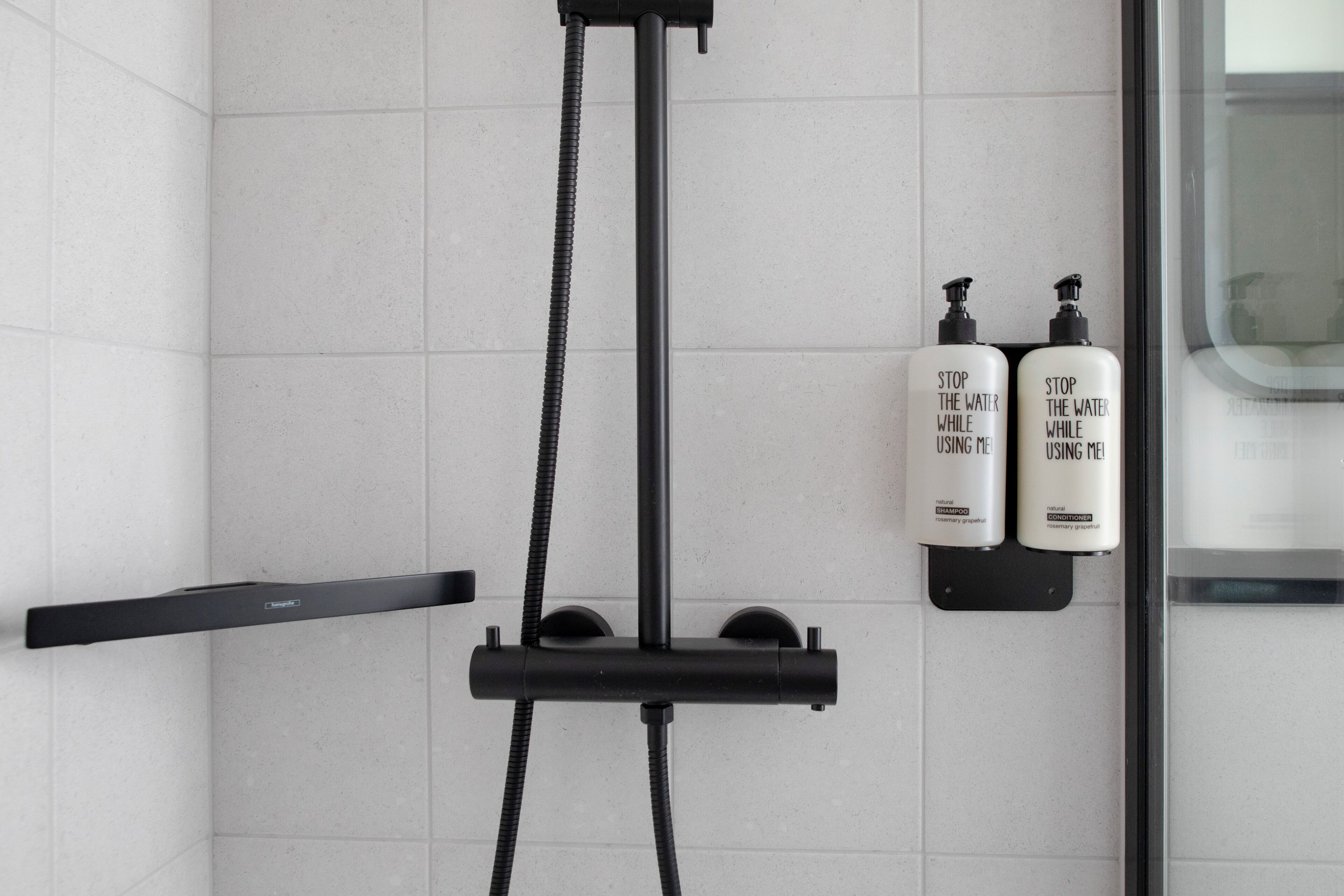 A modern bathroom with a shower, two bottles of shampoo, and a towel rack.