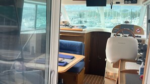 A compact interior with a seating area, a control panel, and a view through a window. - Bateau à Quai (Sainte-Maxime)